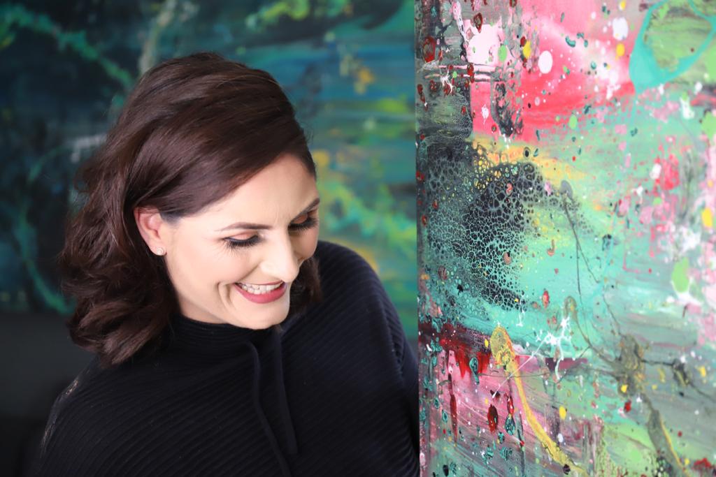 Bild von Sandra lachend neben einem ihrer Kunstwerke